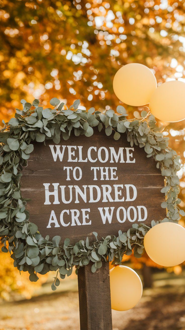 Rustic outdoor wooden sign that reads “Welcome to the Hundred Acre Wood,” surrounded by eucalyptus greenery and yellow balloons, with golden autumn leaves in the background. A charming entrance for a Winnie the Pooh baby shower.